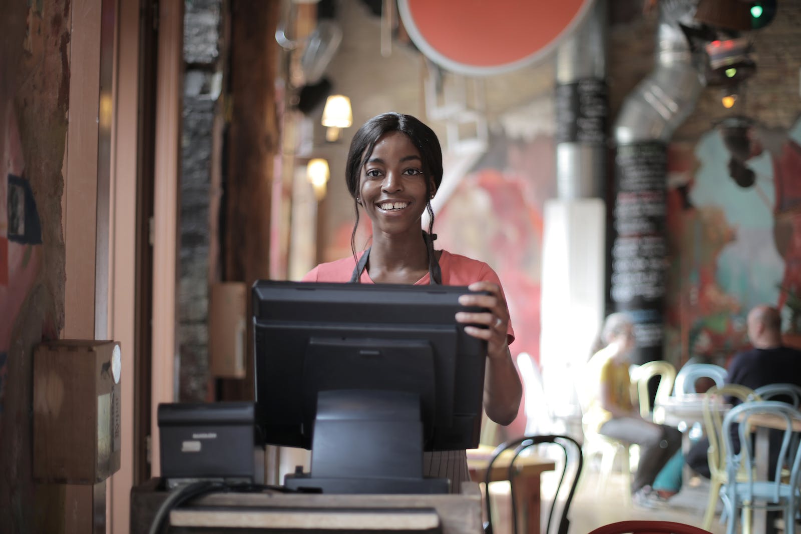 Positive young woman in uniform smiling while standing at counter desk in cafe